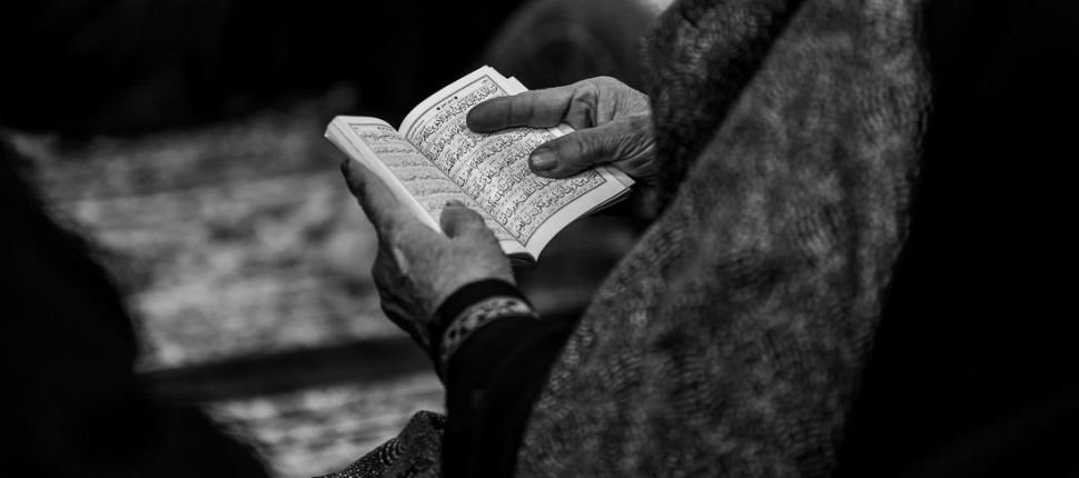 Hands holding an open Qurʾān, in black and white
